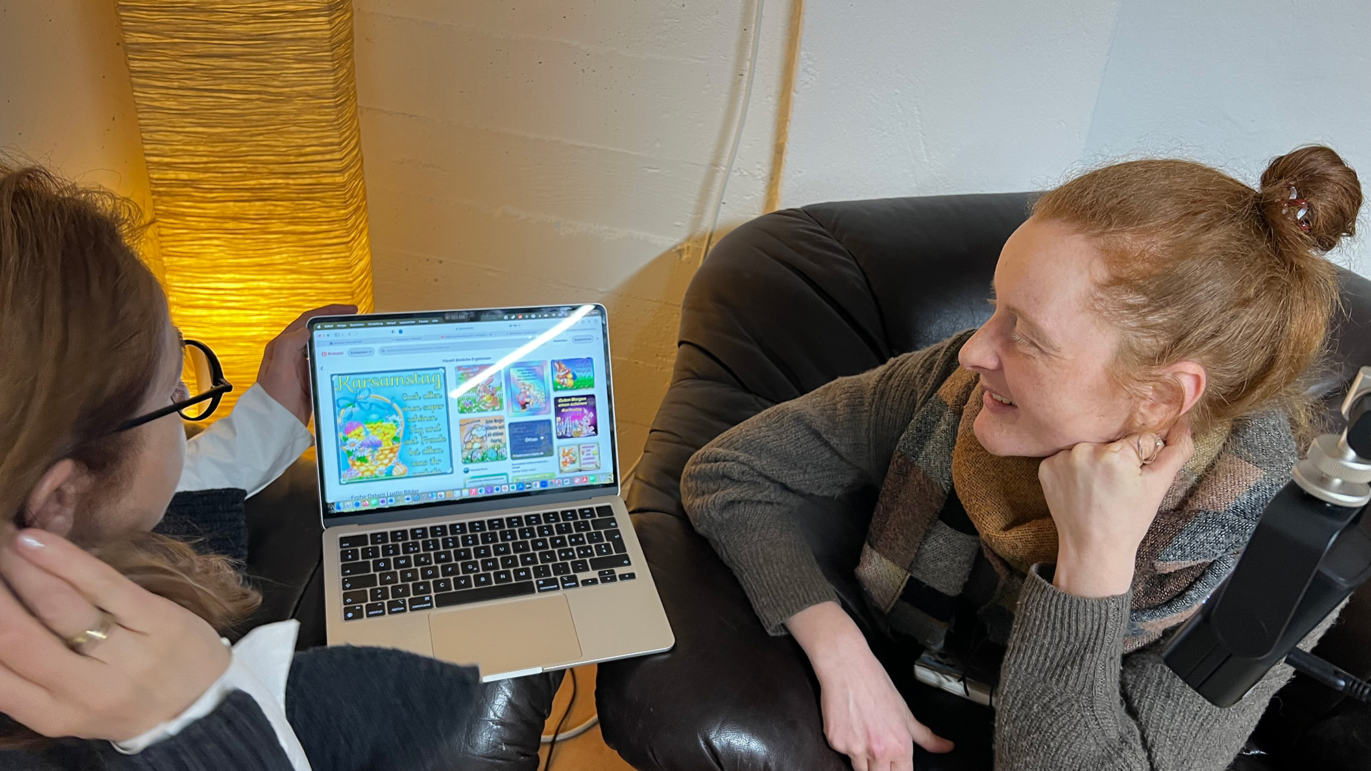 Foto von der Podcast-Aufzeichnung: Zwei Personen schauen auf den Bildschirm eines Laptops, auf dem Bildschrim sieht man Ergebnisse einer Bildersuche, u.a. eine Grusskarte mit gelben Kücken und einer Grussbotschaft