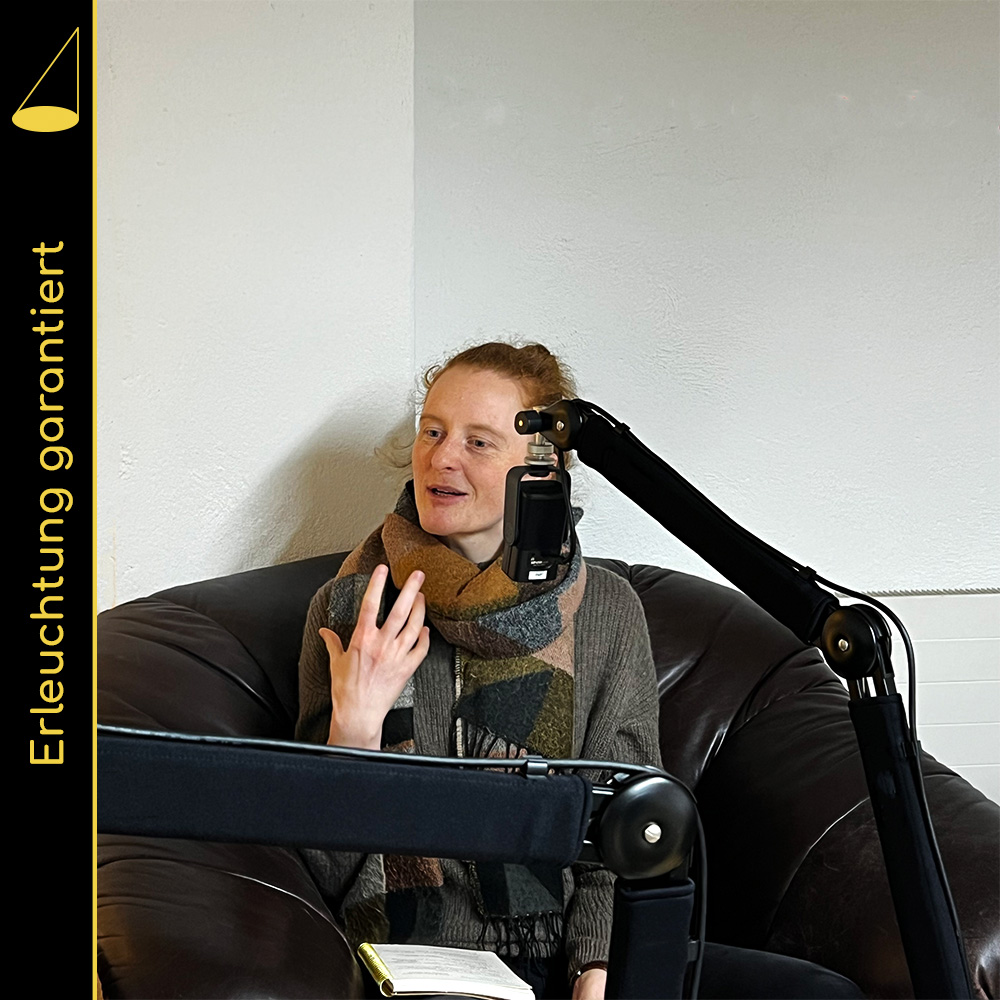 Eine junge Frau sitzt in einem grossen Ledersessel hinter einem Mikrofon und gestikuliert mit der rechten Hand